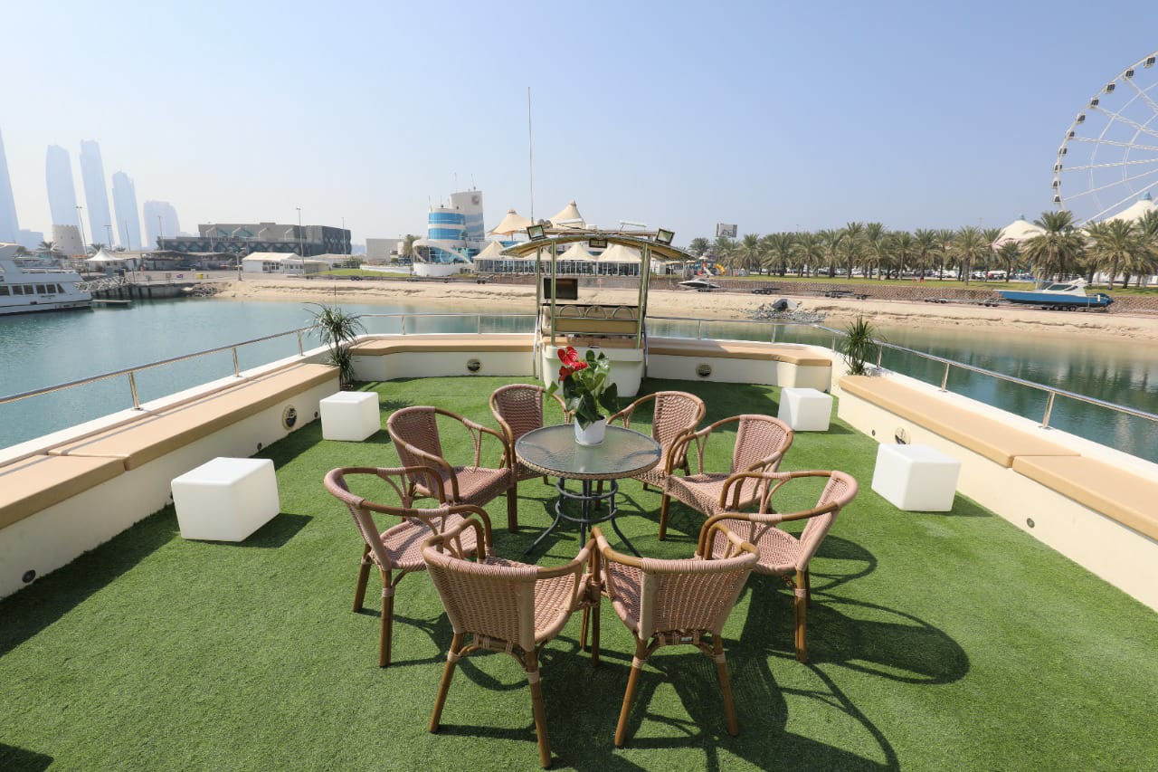 Upper deck with rattan chairs around a table on artificial grass, overlooking the marina