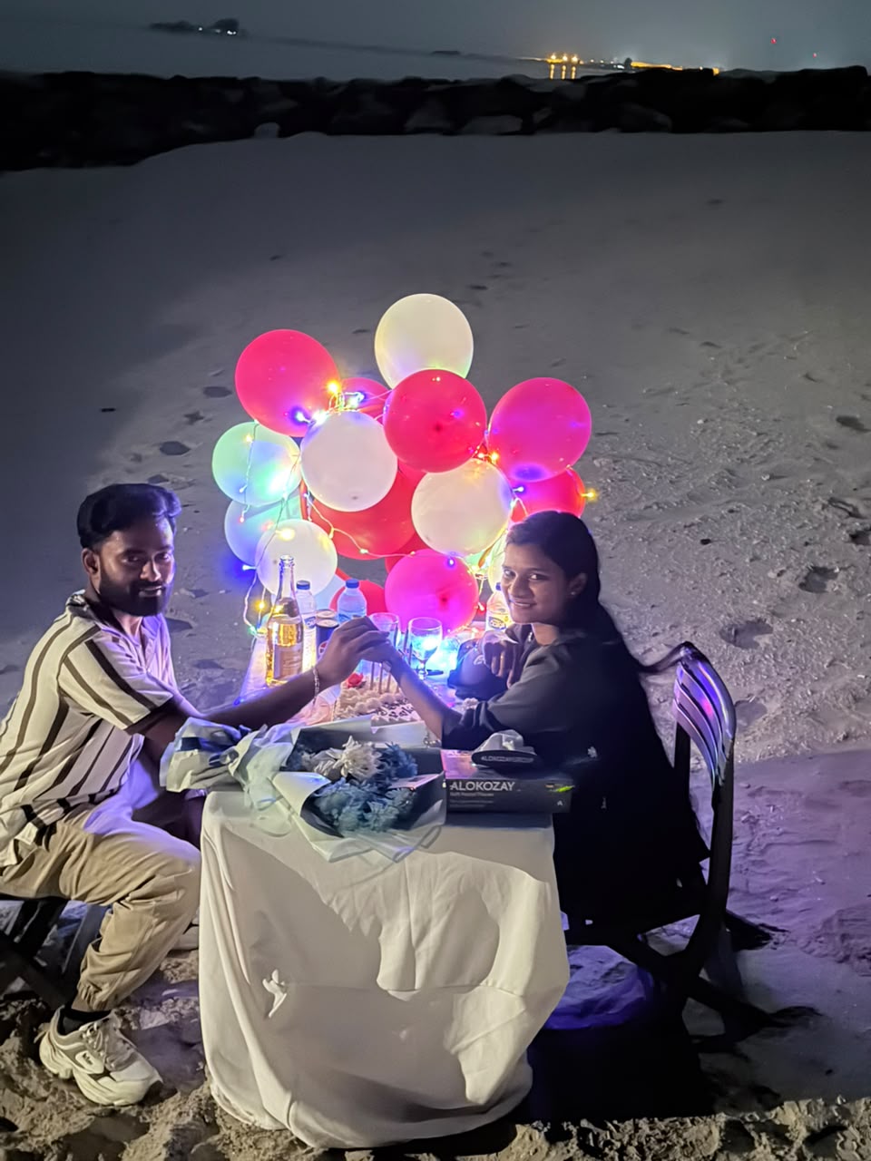Wide view of a romantic birthday beach setup at night with illuminated balloons in Abu Dhabi