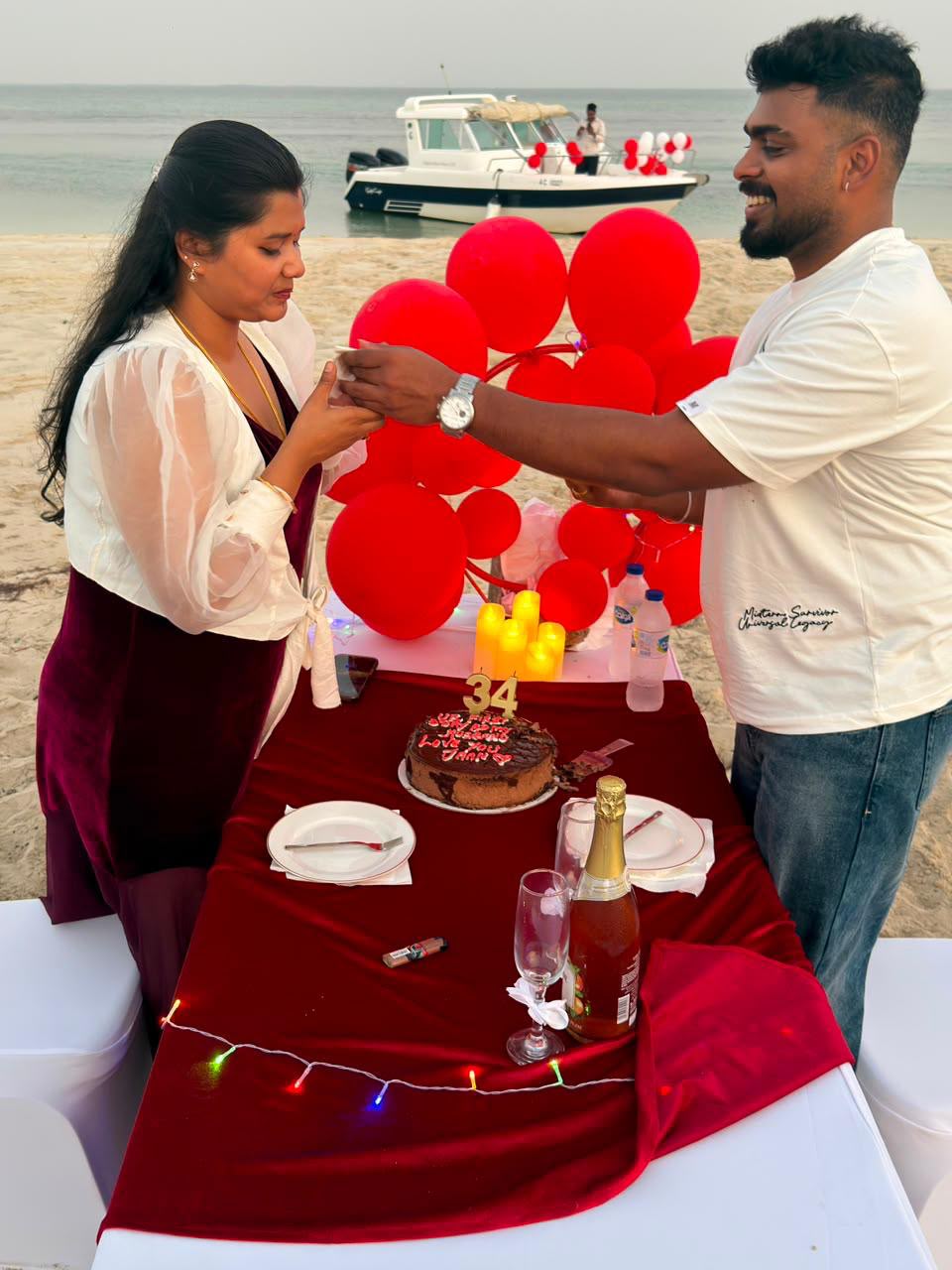 Couple exchanging a birthday toast beside a cake with the charter boat anchored behind them