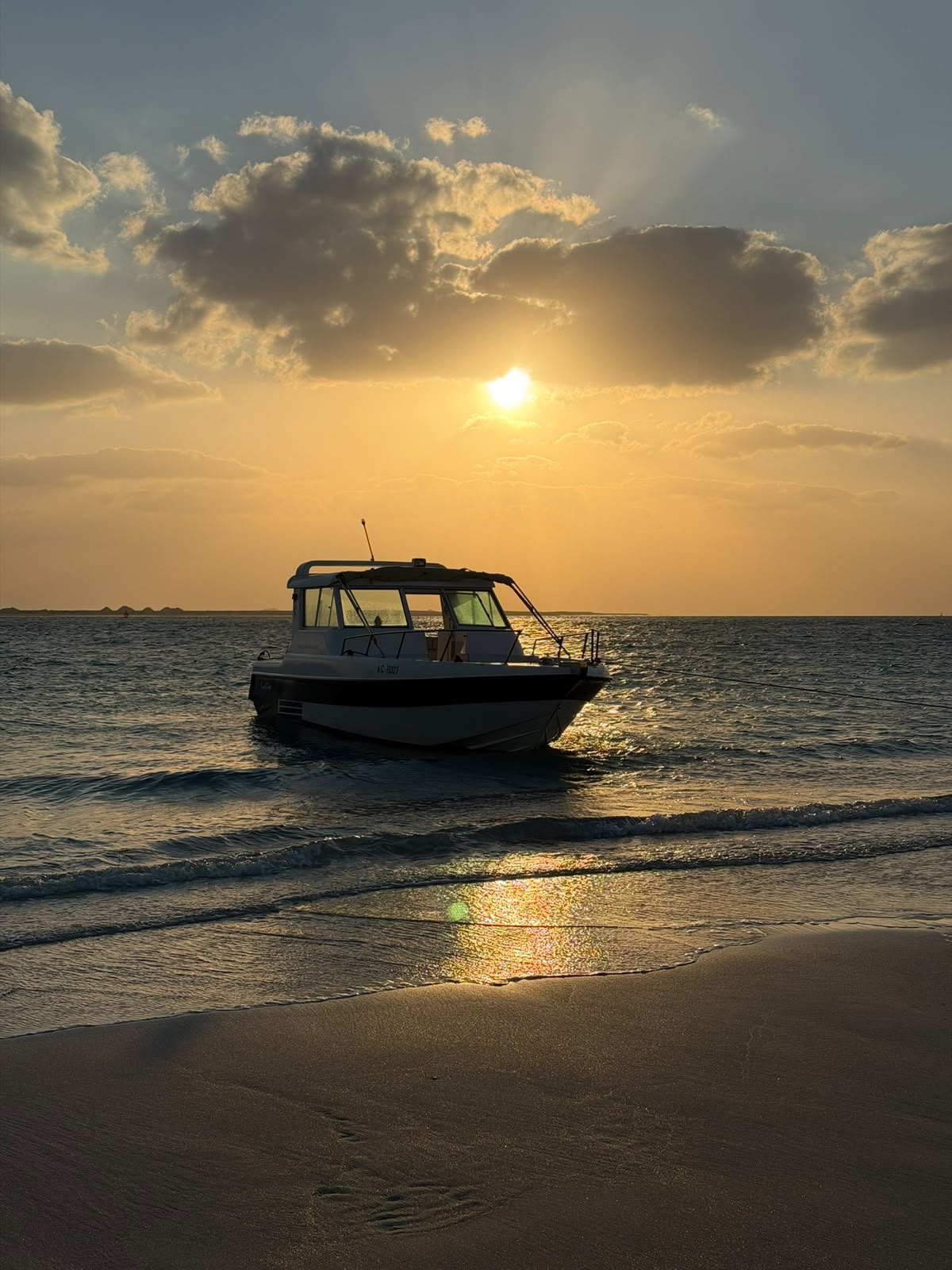 Boat moored just off the beach at sunset, seen from the shoreline