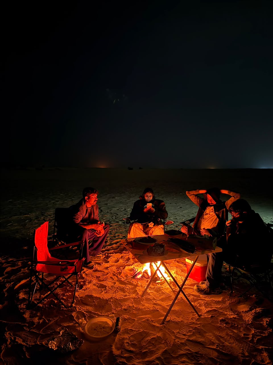 Group of friends gathered around a beach bonfire at night during an island trip