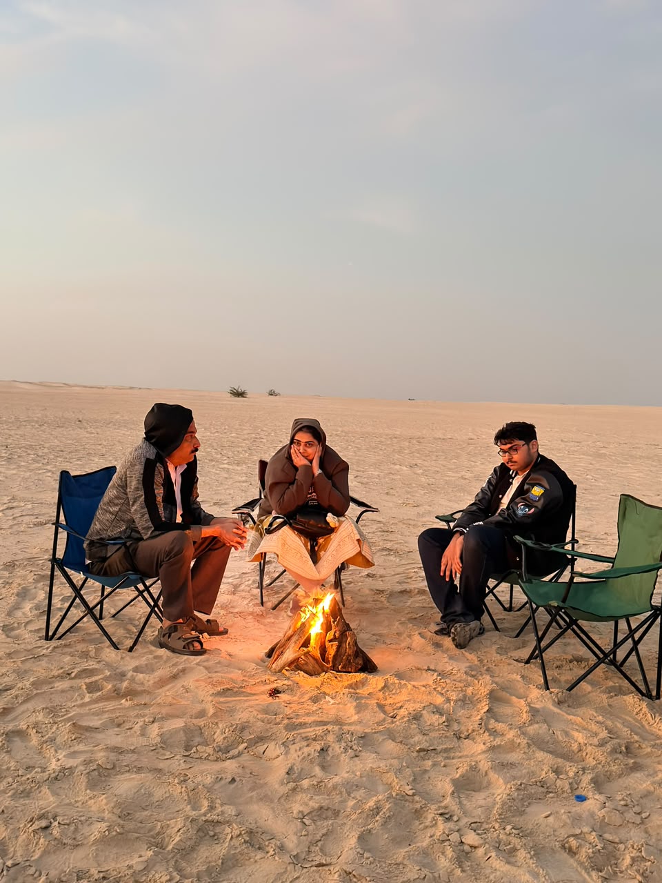 Wide view of friends sitting around a bonfire on open sand dunes at dusk