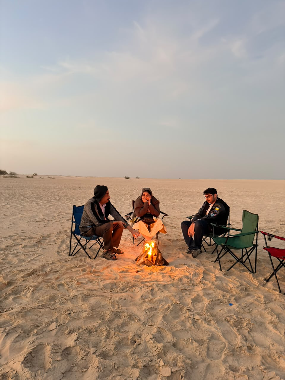 Close view of friends talking around a bonfire on the sand dunes at dusk
