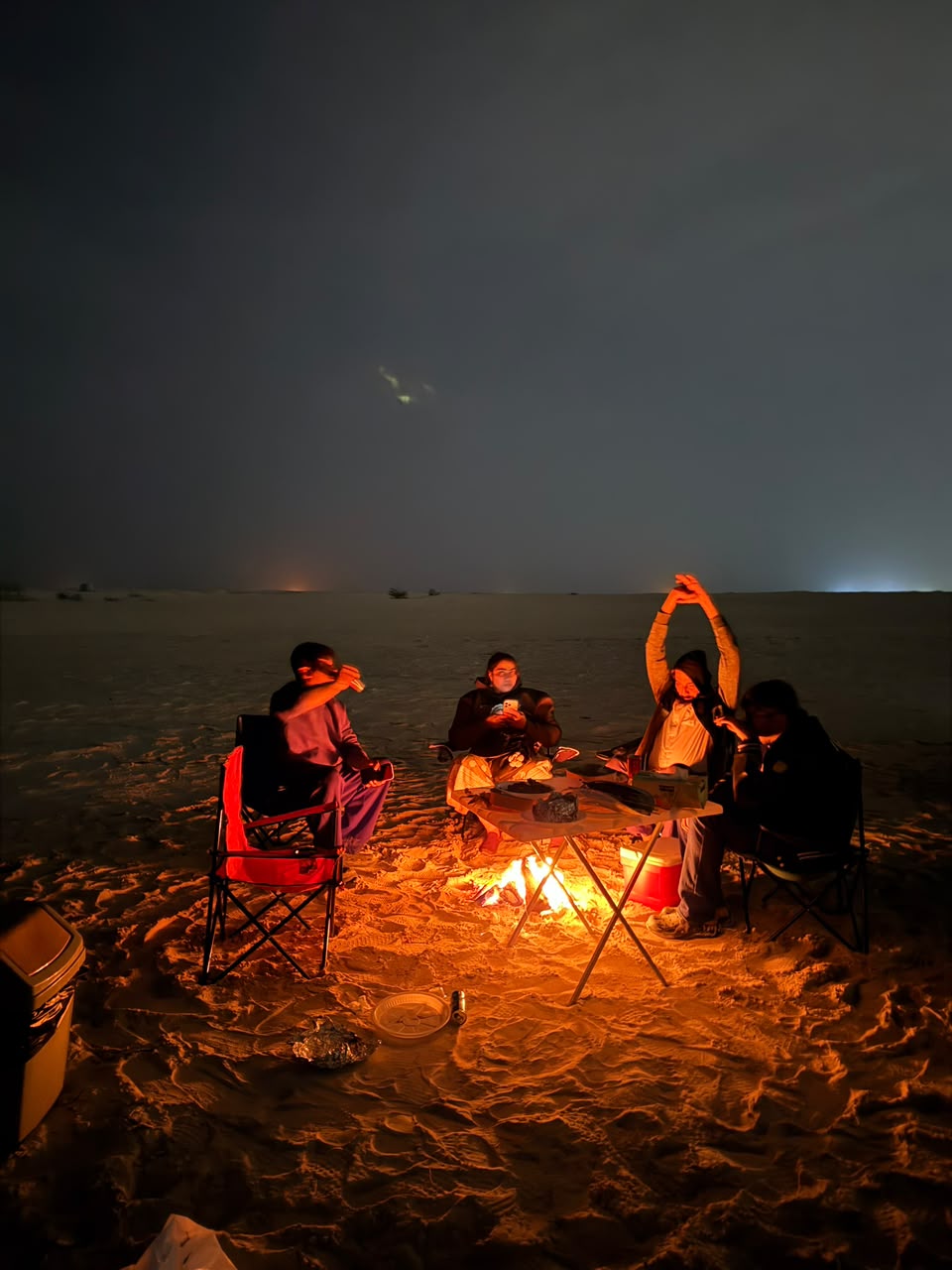 Group celebrating around a beach bonfire at night with one person raising their arms