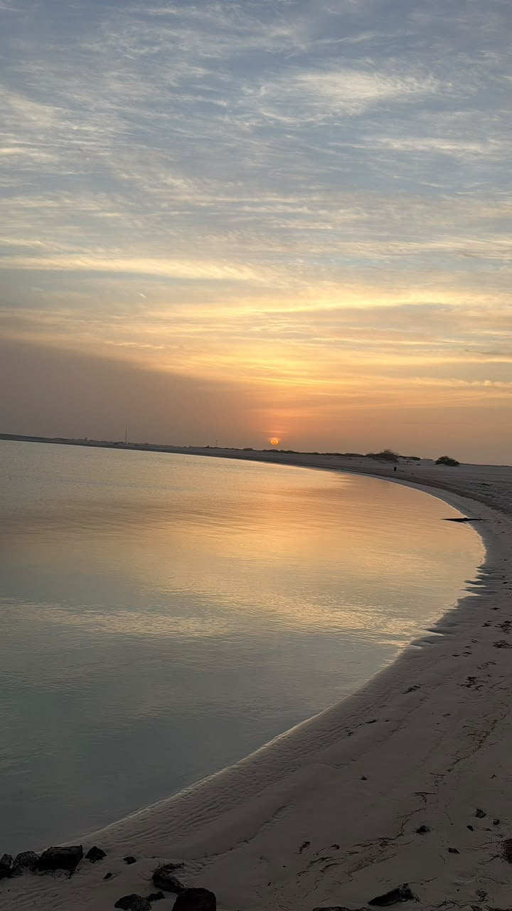 Wide view of a curved Abu Dhabi shoreline reflecting the orange sunset sky