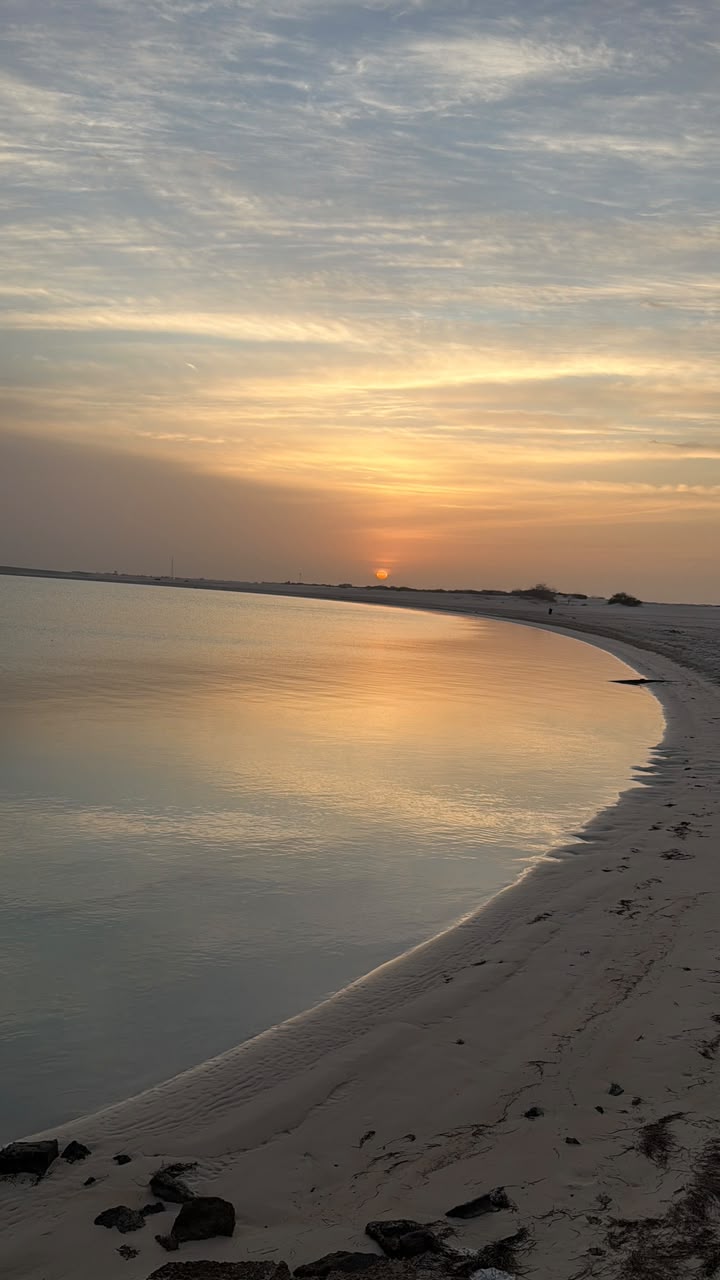 Calm Abu Dhabi shoreline at sunset with the sun low over the water