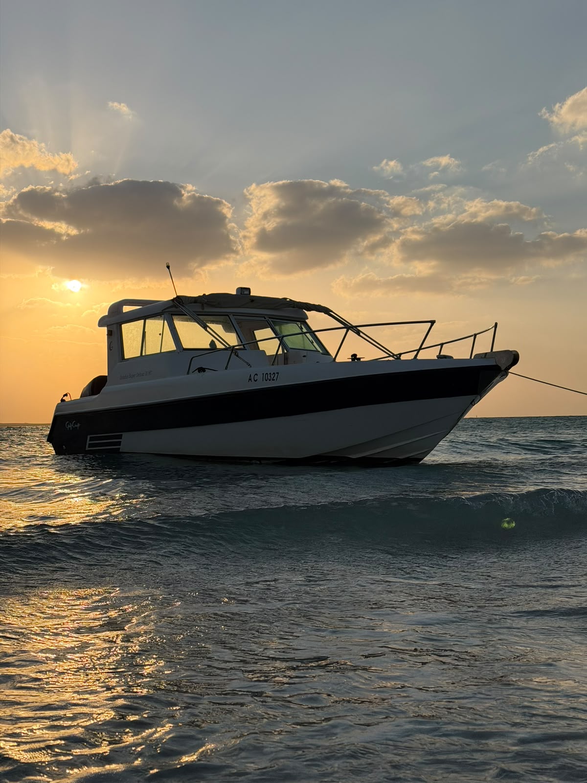 Close-up view of a charter boat at sea with the sun low behind clouds and waves in the foreground
